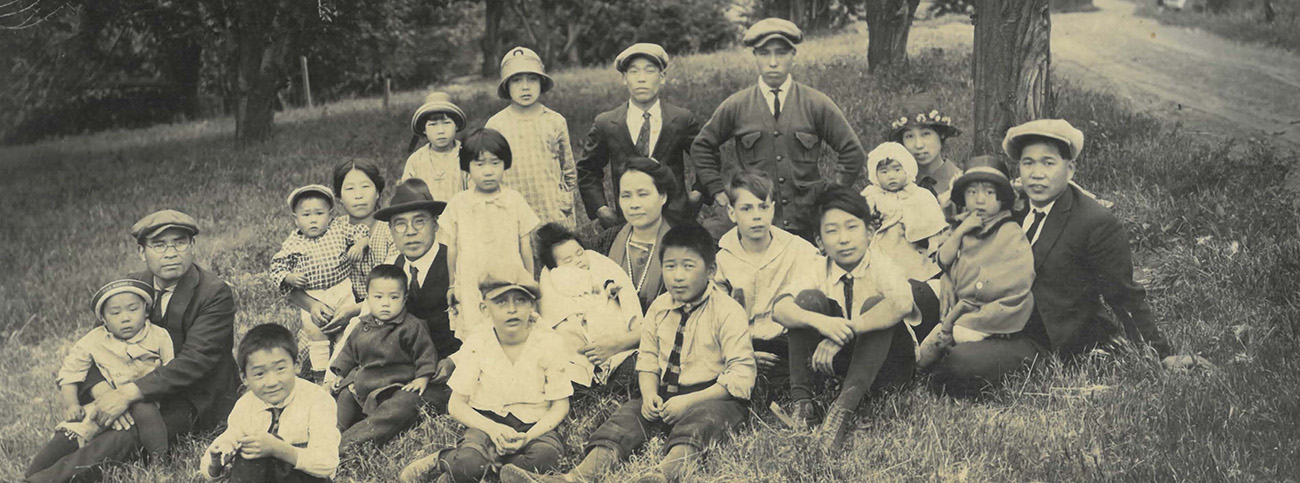 A sepia-toned photograph of a large group of people seated on the grass.
