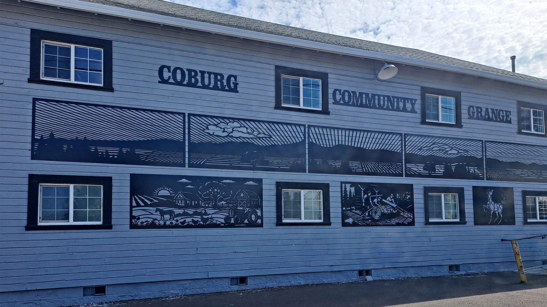 Photograph of a building exterior featuring black and white mural panels depicting various scenes, including wildlife and landscapes.