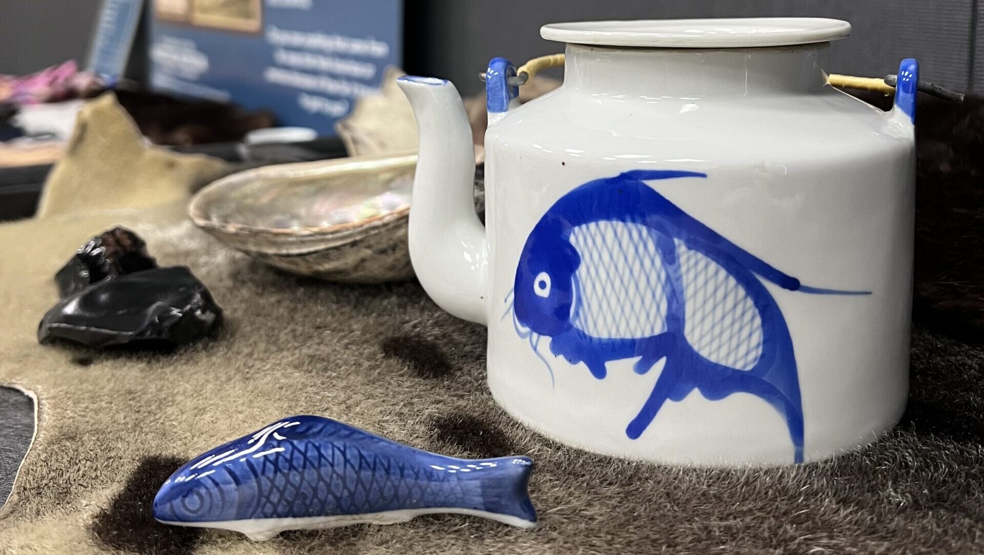 Image of a display at the maritime museum of a ceramic teapot with a blue fish on the side